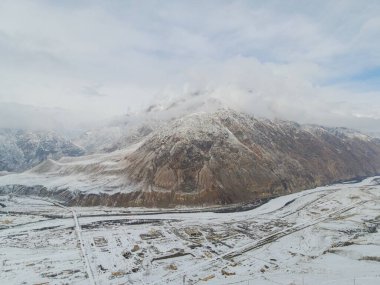 Geniş bir hava manzarası, terk edilmiş Sovyet maden kasabası Enilchek 'i geniş, karla kaplı bir nehir vadisinde, büyük bir dağın eteklerinde yakalıyor.