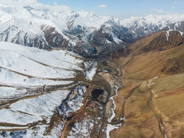 Bir tarafta karla kaplı tepeler diğer tarafta kuru, kahverengi yamaçlar arasında katı bir zıtlık olduğunu gösteren çarpıcı bir dağ vadisi görüntüsü.