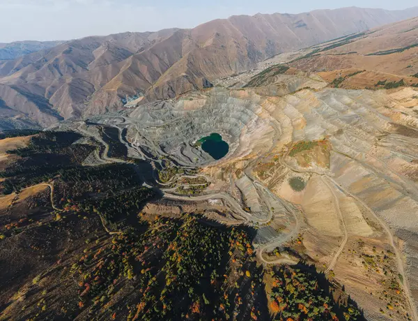 Uçsuz bucaksız, yeşil gölü olan bir açık maden manzarası, sonbahar renklerini gösteren tepeler ve ormanların arasına yerleşmiş.