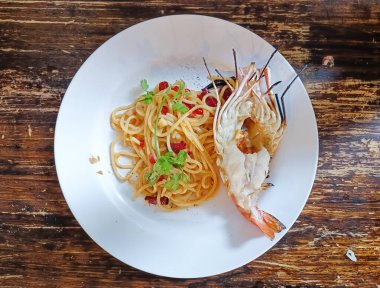 Spagetti ve ızgara karides. Tahta bir masada beyaz bir tabakta.