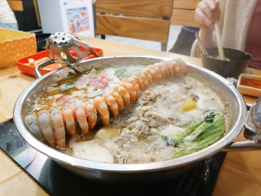 Hot pot with fresh shrimp, sliced meat, vegetables, and boiling soup, perfect for Asian cuisine lovers and authentic dining experiences in a cozy restaurant atmosphere, shabu