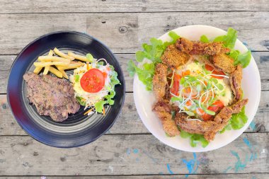 Beyaz tabakta kızarmış domuz etli salata, sağlıklı yemek, siyah tabak, siyah biberli domuz bifteği ve siyah tabakta patates kızartması, ahşap masa. 