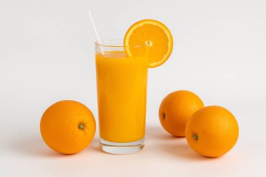 Beyaz arka planda portakallarla çevrili, saman ve portakal dilimli bir bardak taze portakal suyu. Ferahlatıcı ve sağlıklı bir içecek..