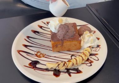 Tatlı bir tatlı sunumu için üzerine krem şanti ve dilimlenmiş muz serpiştirilmiş lezzetli çikolatalı tost. Kafe menüsü, yemek reklamı ve sosyalleşme için mükemmel.