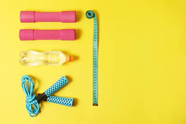 Fitness items jump rope, meter, dumbbells, bottle of water on a yellow background