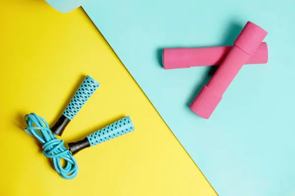 Fitness items, jump rope, dumbbells on a yellow and blue background