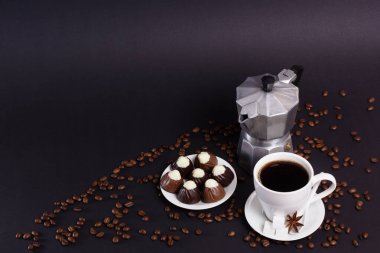 Bir fincan kahve bir espresso makinesi ve küçük bir tabak şekerin yanında oturur. Kahve çekirdekleri koyu bir yüzeye yayılmış ve kopyası için yer açılmış..