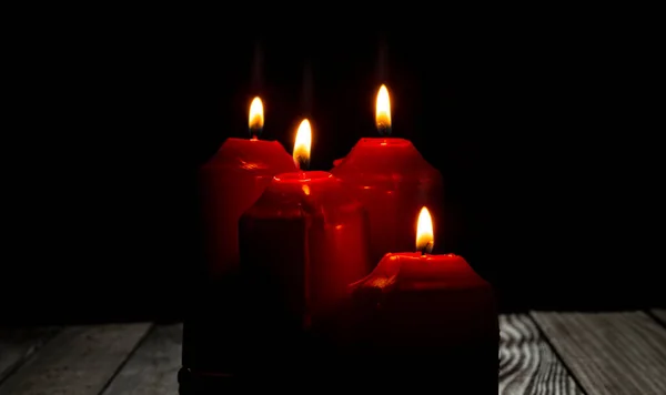 Four red candles light on dark room with dark background.