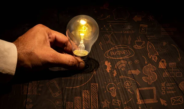 手握带有图标的灯泡的人 桌上创业业务理念 — 图库照片