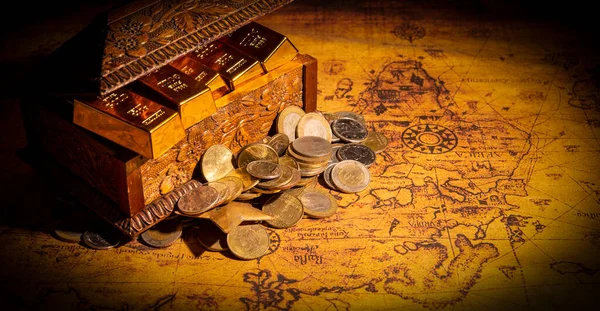 Dünya haritasında altın külçeleri ve sikkelerle dolu antika bir hazine kutusu. Keşif kavramı.