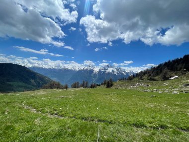 İtalyan Alpleri 'nin hava manzarası, arka planda karla kaplı tepeler, mavi gökyüzü ve beyaz bulutlar.