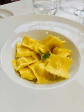 Beyaz bir tabakta servis edilen, bol kahverengi soslu ve taze maydanozla süslenmiş gurme ravioli.