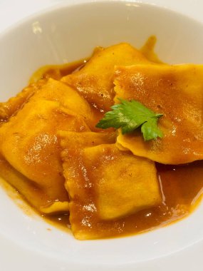 Beyaz bir tabakta servis edilen, bol kahverengi soslu ve taze maydanozla süslenmiş gurme ravioli.