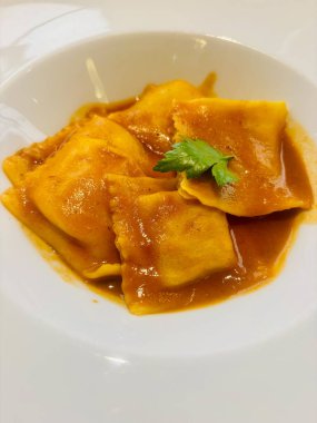 Beyaz bir tabakta servis edilen, bol kahverengi soslu ve taze maydanozla süslenmiş gurme ravioli.