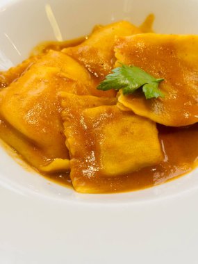 Beyaz bir tabakta servis edilen, bol kahverengi soslu ve taze maydanozla süslenmiş gurme ravioli.