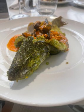 Bitkilerle kaplı fırında balık, midye ve midyeli domates sosu ile kaplanmış..