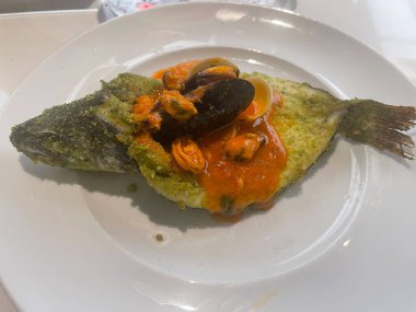 Bitkilerle kaplı fırında balık, midye ve midyeli domates sosu ile kaplanmış..