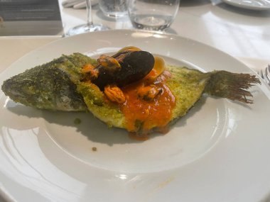 Bitkilerle kaplı fırında balık, midye ve midyeli domates sosu ile kaplanmış.