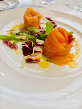 Zarif tütsülenmiş somon rulolarının bulunduğu rafine bir yemek. Taze salatadan yapılmış bir yatakta ustalıkla hazırlanmış.