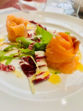 Zarif tütsülenmiş somon rulolarının bulunduğu rafine bir yemek. Taze salatadan yapılmış bir yatakta ustalıkla hazırlanmış.