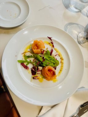 Zarif tütsülenmiş somon rulolarının bulunduğu rafine bir yemek. Taze salatadan yapılmış bir yatakta ustalıkla hazırlanmış.