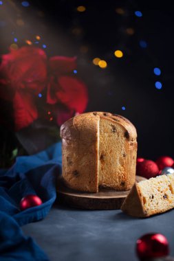 Bir parça panettone tatlı ekmek, geleneksel İtalyan yemeği. Karanlık bir arka planda, masada kutsal ve çelenk var.