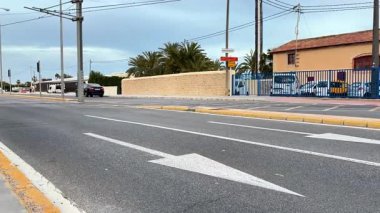 Alicante, İspanya - 25 Nisan 2025: Bir araba palmiye ağaçları ve canlı duvar resimleriyle dolu huzurlu bir yolda ilerliyor. Güneş arka planda batar ve pitoresk bir şehir atmosferi yaratır. Burası.