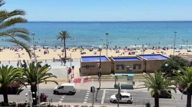 Alicante, İspanya - 29 Mayıs 2025: Açık mavi sular ziyaretçileri eğlenceli bir gün için cezbettiği için aileler ve arkadaşlar kumlu sahilde dinleniyor. Renkli şemsiyeler sıcak ve güneşli bir öğleden sonra sahili işaret ediyor..