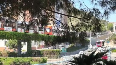 Canlı bir şehir manzarası modern bir ulaşım sistemini gözler önüne seriyor. Yukarıda, araçlar aşağıdaki hareketli yollarda ilerlerken yeşil alanda bir geçiş hattı süzülüyor..