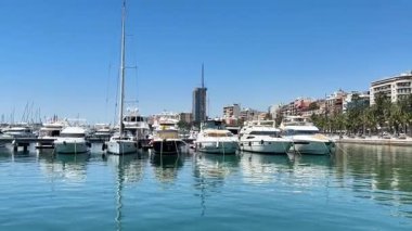 Alicante, İspanya - 29 Mayıs 2025: Şok edici bir rıhtıma karşı hizaya gelmiş canlı bir yat sergileniyor. Açık mavi gökyüzü limanı aydınlatıyor, mükemmel bir yaz günü sunuyor..