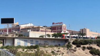 Ziyaretçiler canlı bir atmosfer yaşıyorlar Alicante, İspanya - 29 Mayıs 2025: Alc Campo alışveriş merkezi, açık mavi gökyüzü altındaki mağazalar ve restoranlarla çevrili, bu da burayı herkes için davetkar bir yer yapıyor.