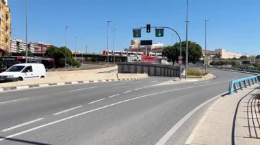 Avenida de la Bahia Alicante, İspanya 'da yoğun trafik akışı - 29 Mayıs 2025: açık mavi gökyüzü altında, yeşil trafik sinyalleri şehre doğru yumuşak bir hareket olduğunu gösteriyor. Kenti çevreleyen