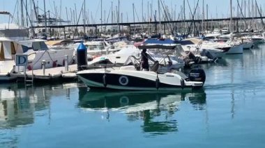 Alicante, İspanya - 29 Mayıs 2025: Bir zevk teknesi marina sularında sayısız yat ve yelkenliyle sorunsuzca süzülüyor. Canlı sahne, sakin yansımalarla güneşli bir günü betimliyor.