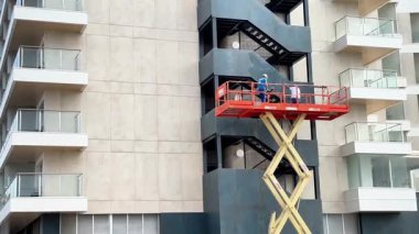 Alicante, İspanya - 3 Haziran 2025: Makas asansörlü işçiler, güvenlik ve işbirliğini vurgulayarak çağdaş bir binanın dış yüzeyini koruyorlar