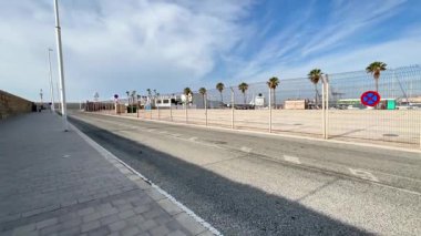 Alicante, İspanya - Haziran 03, 2025: Sarı otobüs açık mavi gökyüzü altında palmiye ağaçlarıyla kaplı kıyı yolunda ilerliyor, canlı bir yolculuk ortamı yaratıyor.