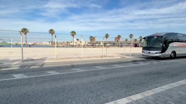 Alicante, İspanya - 3 Haziran 2025: Sahil şeridi, güneşli bir sahil gününde canlı bir atmosfer yaratan palmiye ağaçları ve çitlere sahiptir.