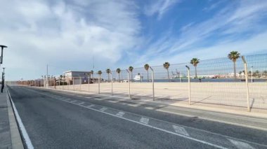 Alicante, İspanya - 3 Haziran 2025: Palmiye ağaçları ve çitlerle dolu deniz manzarası, açık gökyüzü ve uzak binalar, seyahat görüntüleri için mükemmel