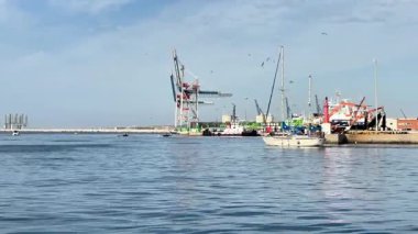 Alicante, İspanya - 3 Haziran 2025: Sahil teknesi turna ve konteynırlarla dolu hareketli limanın yanında sakin sularda geziniyor