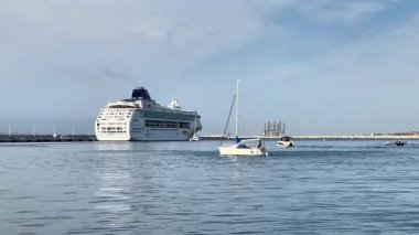 Alicante, İspanya - 3 Haziran 2025: Büyük yolcu gemisi, ön planda küçük teknelerle sakin sularda yüzüyor, pitoresk bir liman ayarını vurguluyor.