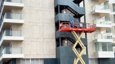 Alicante, İspanya - 3 Haziran 2025: Makas asansörlü işçiler, güvenlik ve işbirliğini vurgulayarak çağdaş bir binanın dış yüzeyini koruyorlar