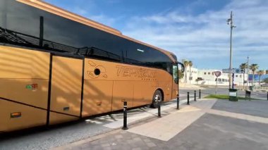 Alicante, İspanya - 3 Haziran 2025: Palmiye ağaçları ve açık mavi gökyüzü ile çevrili istasyondan ayrılan otobüs, kentsel ulaşım ve seyahatleri vurguluyor