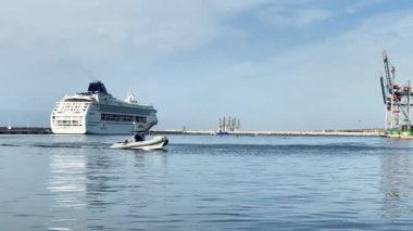 Alicante, İspanya - 3 Haziran 2025: Büyük yolcu gemisi limanda demirlerken, küçük motorlu tekne berrak gökyüzü altında sakin sularda yüzüyor