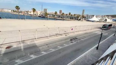 Alicante, İspanya - 3 Haziran 2025: Sahil yolunda palmiye ağaçları ve sakin bir sahil kenti güzelliği ve boş zamanlarını ön plana çıkaran bir otobüs yer alıyor.