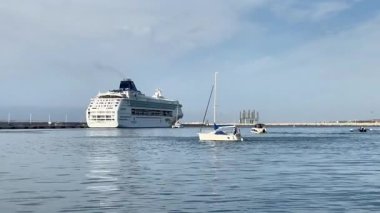 Alicante, İspanya - 3 Haziran 2025: Büyük yolcu gemisi, ön planda küçük teknelerle sakin sularda yüzüyor, pitoresk bir liman ayarını vurguluyor.