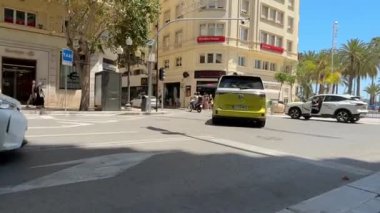 Alicante, İspanya - 30 Mayıs 2025: Siyah lüks araba yayalar ve binalarla güneşli bir caddede dönüyor, kentsel yaşam tarzı ve mimarisini ön plana çıkarıyor