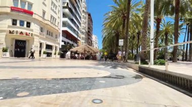 Alicante, İspanya - 30 Mayıs 2025: Canlı şehir meydanı insanlarla dolu canlı bir şehir atmosferi yaratan palmiye ağaçları, açık kafe ve modern binalar içerir.