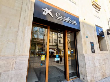 Alicante, İspanya - 24 Haziran 2025: CaixaBank girişi ahşap kapılı ve berrak markalı çağdaş tasarım içeriyor.