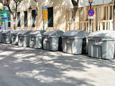 Alicante, İspanya - 24 Haziran 2025: Modern gri çöp bidonları kentsel cadde boyunca düzenli olarak düzenlenmekte olup, etkili atık imhası ve şehir organizasyonunun altını çizmektedir