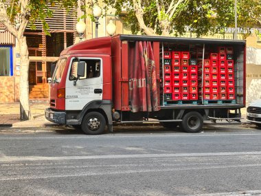 Alicante, İspanya - 24 Haziran 2025: Canlı kırmızı kasalarla dolu caddeye park edilmiş teslimat aracı, kentsel ulaşım ve lojistiği vurguluyor