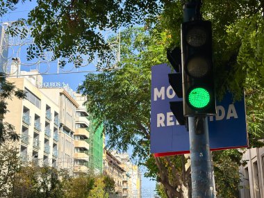 Alicante, İspanya - 24 Haziran 2025: Yeşil trafik sinyali Santiago 'da işlek bir caddeden, kentsel mimari ve yemyeşil ağaçlarla güvenli bir geçiş olduğunu gösteriyor